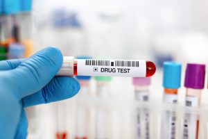 Gloved hand holding a sample tube labeled Drug Test
